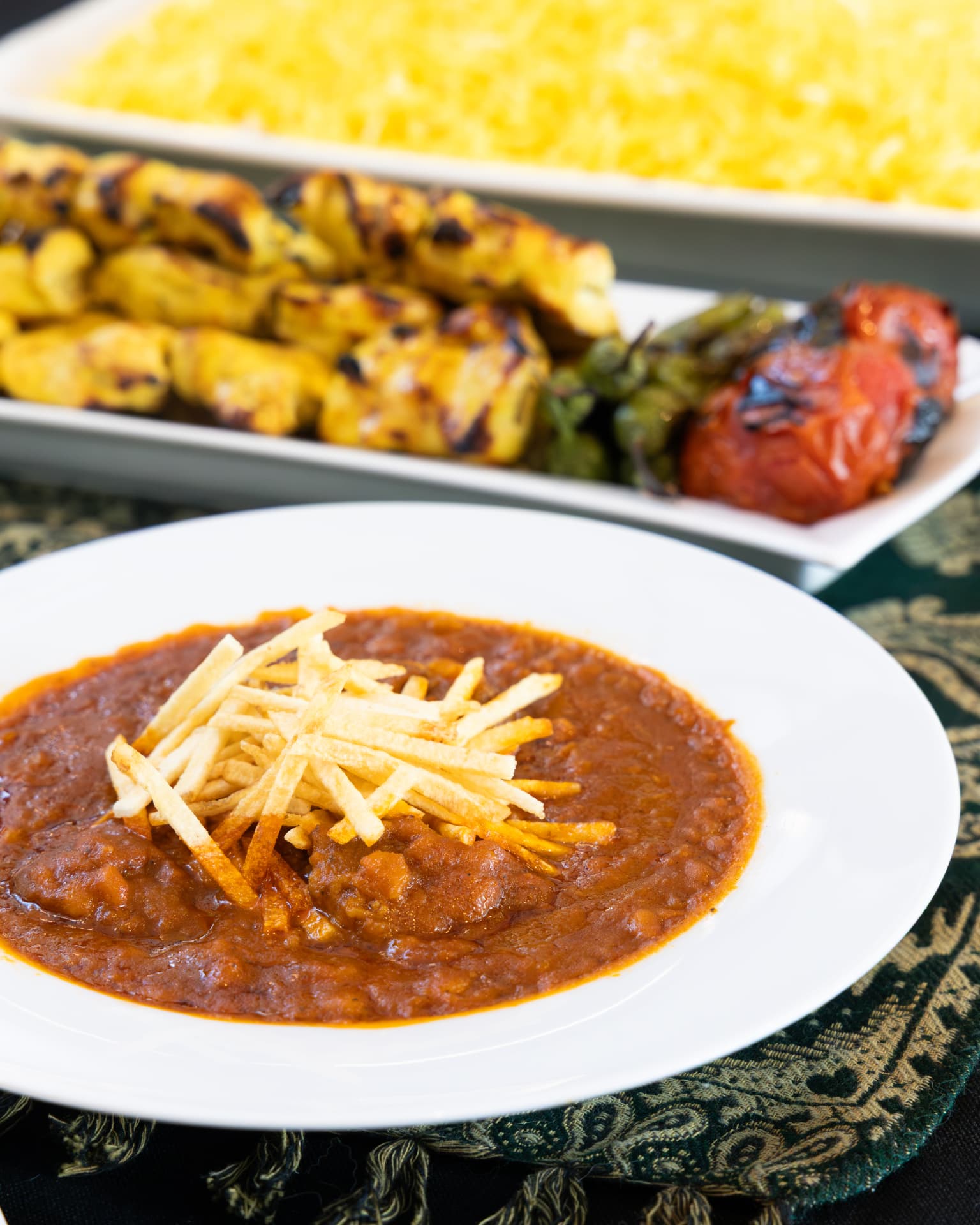 Gheymeh stew topped with crispy shoestring fries, with joojeh kabob and saffron rice behind