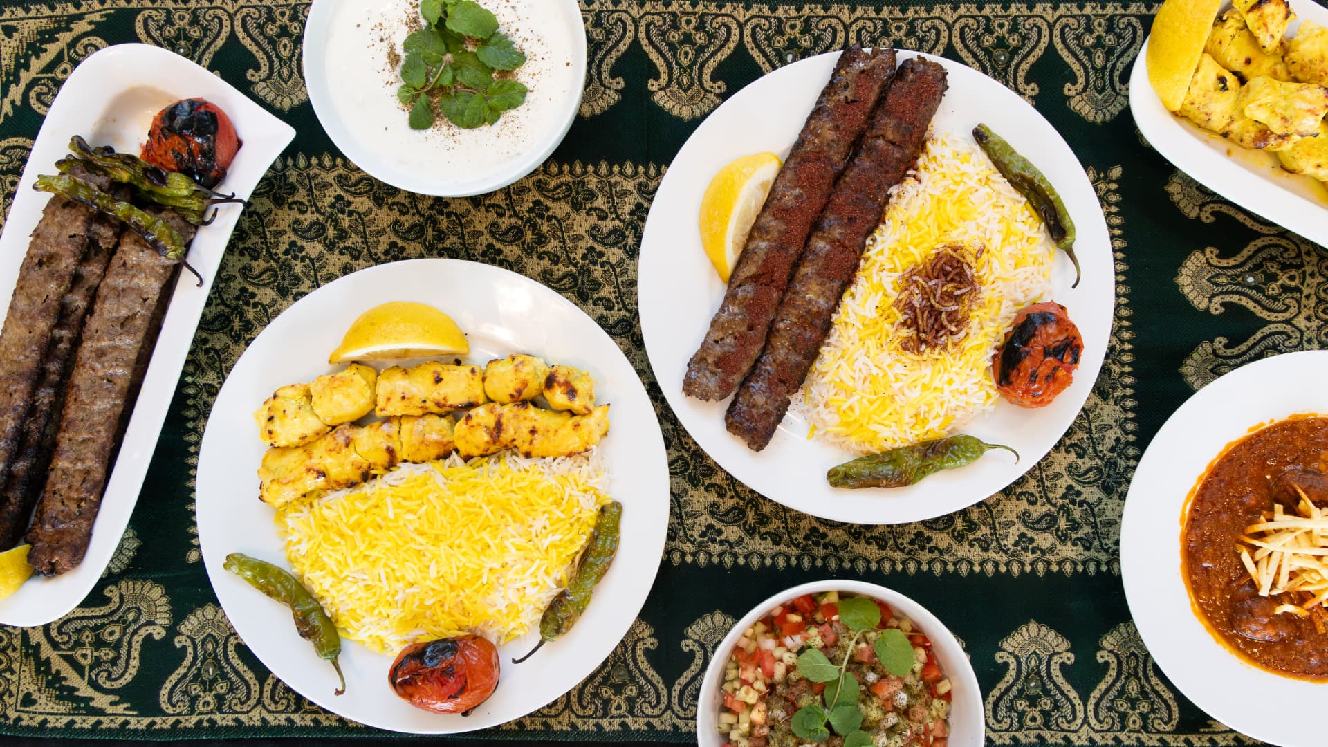 An overhead Persian spread with joojeh and koobideh kabobs, gheymeh, lavash, mast-o-khiar, and salad Shirazi