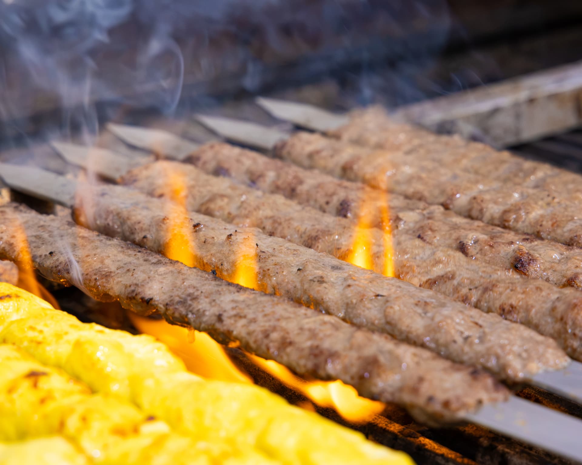 Koobideh kabobs cooking over open flame on flat skewers